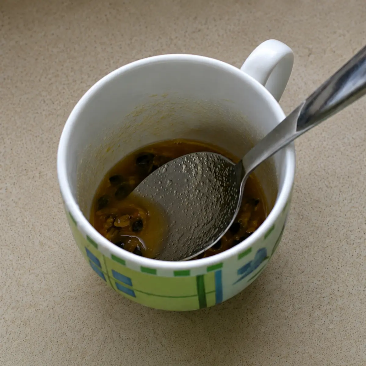 Passion fruit coulis with seeds mixed in a cup with a spoon.
