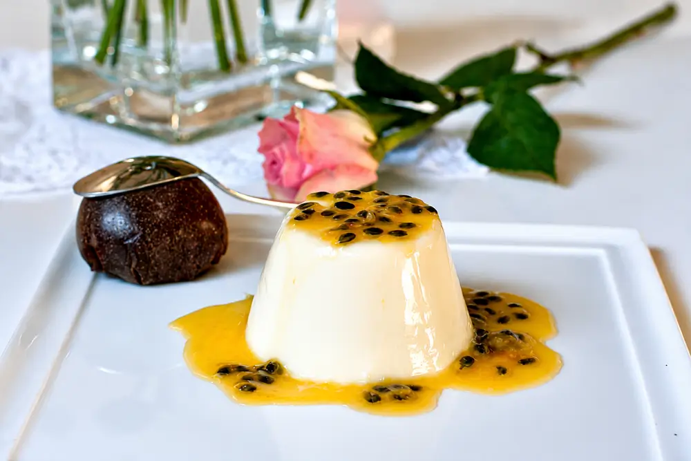 Passion Fruit Panna Cotta with Vanilla Cream served with glossy passion fruit coulis on a white plate.