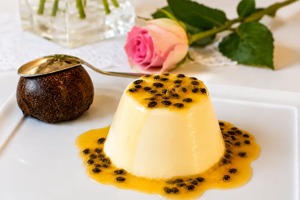 Vanilla Panna Cotta with Passion Fruit Coulis Passion Fruit Panna Cotta with Vanilla Cream served with fresh passion fruit coulis on a white plate.