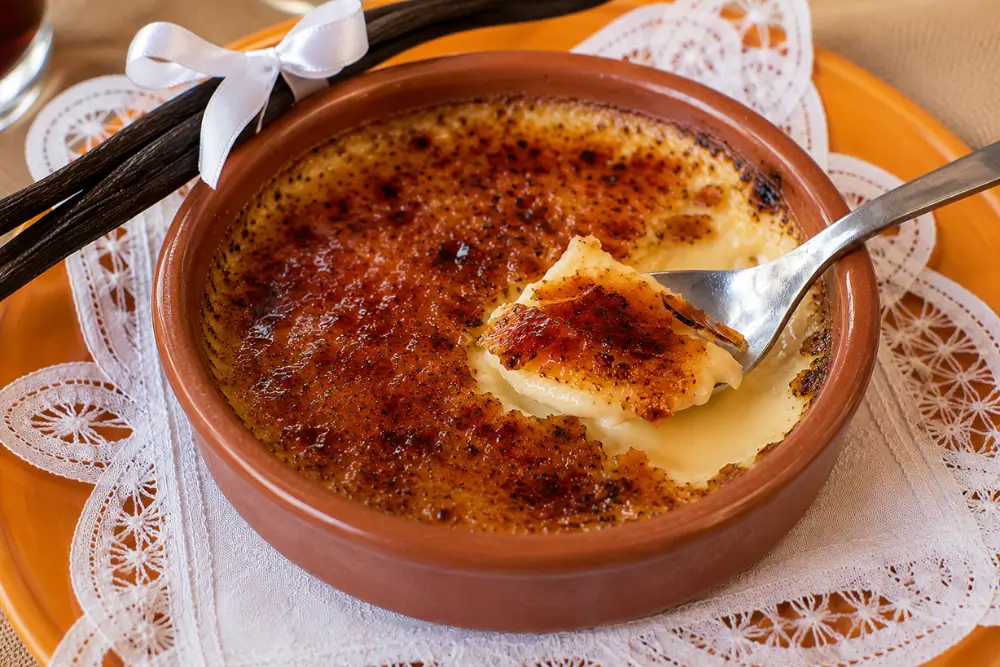 Spoon lifting creamy vanilla custard and crisp caramel topping from freshly made crème brûlée.