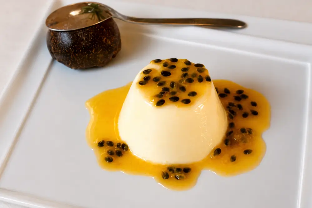 Vanilla panna cotta topped with glossy passion fruit coulis and fresh passion fruit seeds.