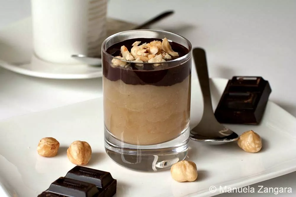 Maple Pear Mousse Shooters with Chocolate and Hazelnuts Single glass of pear mousse topped with melted dark chocolate and chopped hazelnuts on a white plate with chocolate squares.
