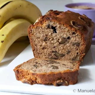 Sliced banana walnut bread with walnuts through the crumb beside fresh bananas.