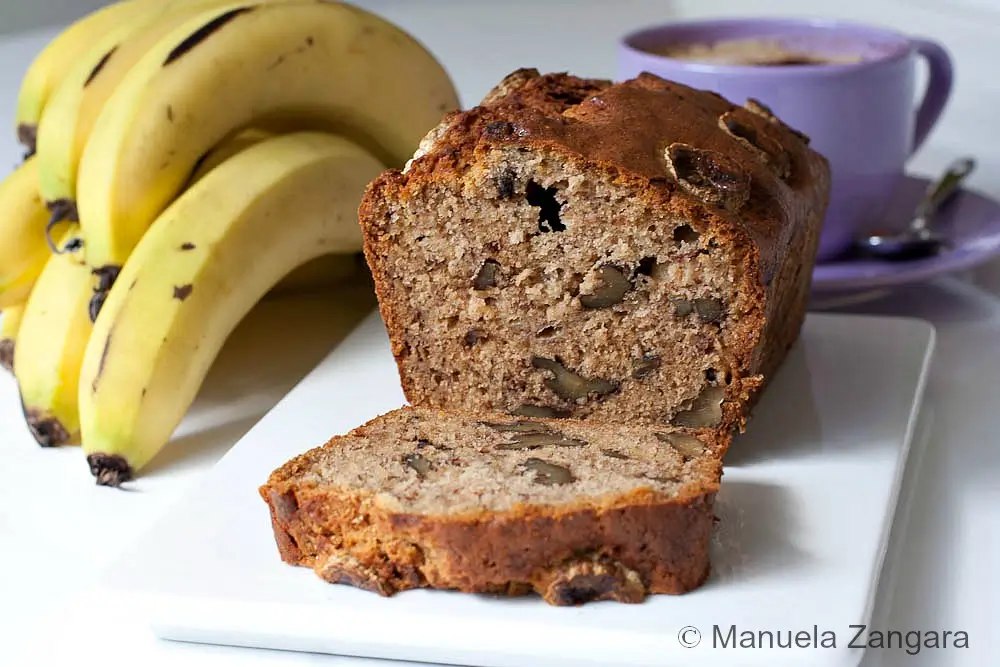 Walnut Banana Bread Sliced banana walnut bread with walnuts through the crumb beside fresh bananas.
