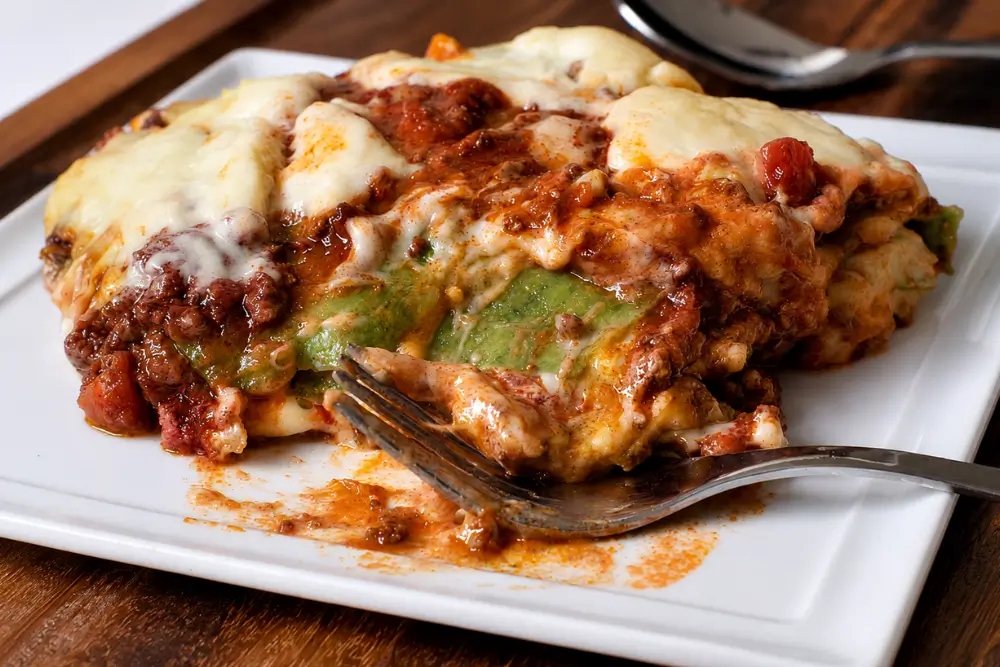 Slice of Lasagne Verdi with green pasta, ragù, and melted mozzarella on a white plate.