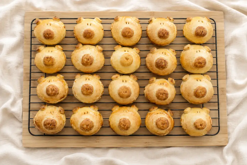 Homemade pig-shaped buns arranged in rows on a cooling rack.