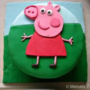 Peppa Pig fondant cake base covered in green and blue fondant with Peppa’s face placed on top before adding final decorations.