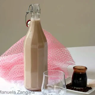 Bottle of homemade Baileys Irish Cream with a glass and coffee syrup on the side.
