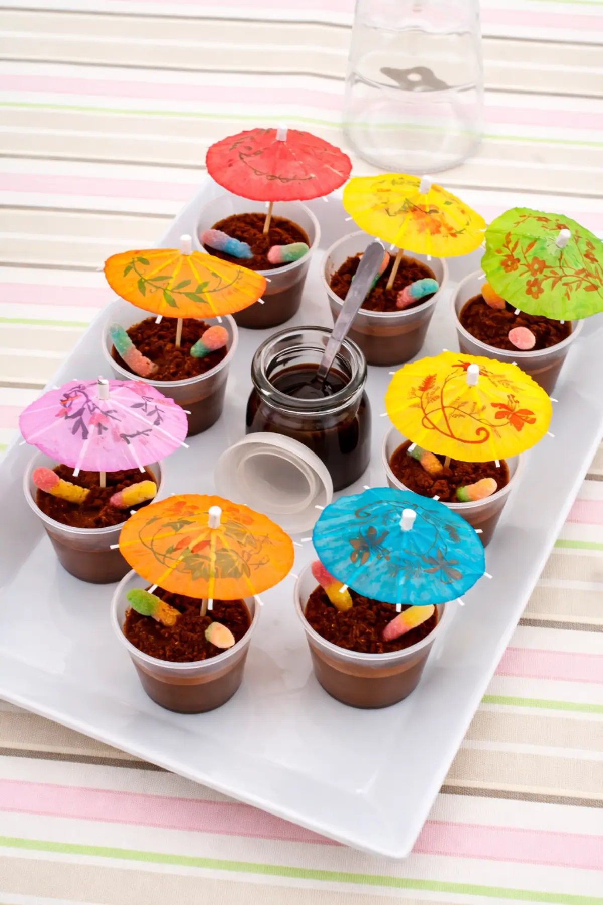 Chocolate pudding cups topped with crumbs, gummy worms, and bright umbrellas on a serving tray.