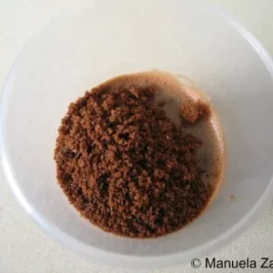 Overhead shot of chocolate panna cotta topped with crushed cookie crumbs in a clear cup.
