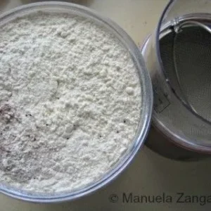 A bowl of sifted flour and cocoa powder with a sieve beside it.