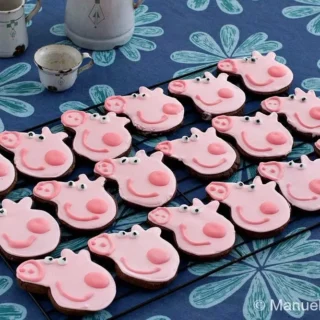 A full tray of decorated Peppa Pig Chocolate Cookies displayed on a patterned tablecloth.