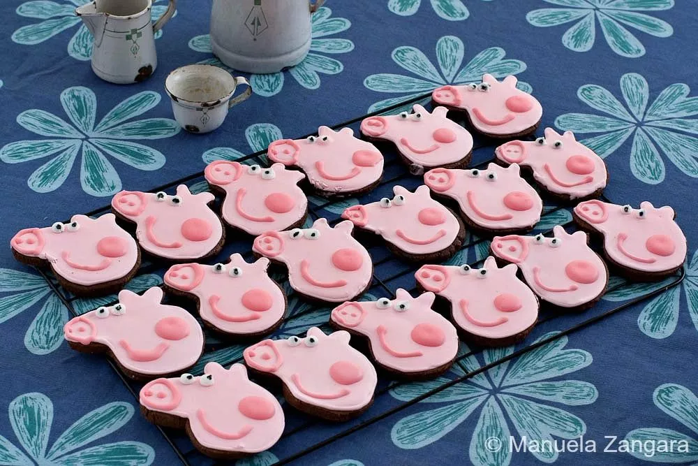 A full tray of decorated Peppa Pig Chocolate Cookies displayed on a patterned tablecloth.