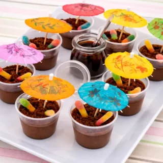 Peppa Pig Muddy Puddle Cups decorated with biscuit crumbs, gummy worms, and colourful paper umbrellas.