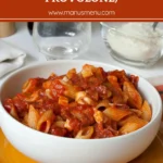 Bowl of penne in rich tomato sauce with pieces of salami and melted cheese.