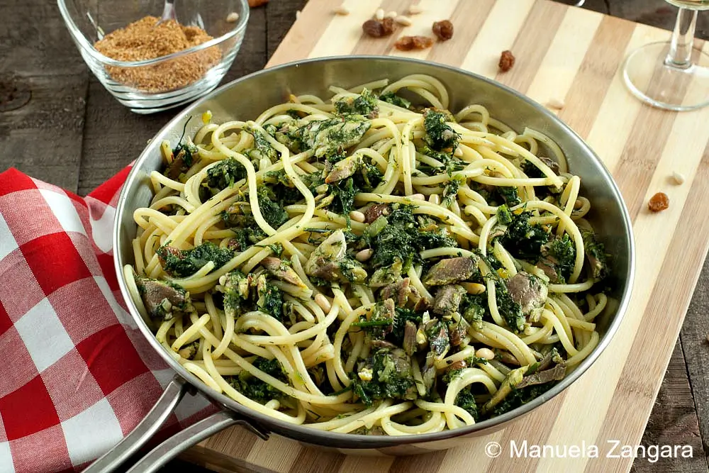 Close-up of bucatini mixed with sardines, fennel, raisins, and pine nuts in a stainless-steel pan.