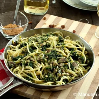 Finished bucatini with sardines and fennel in a pan, served with wine and toasted breadcrumbs.