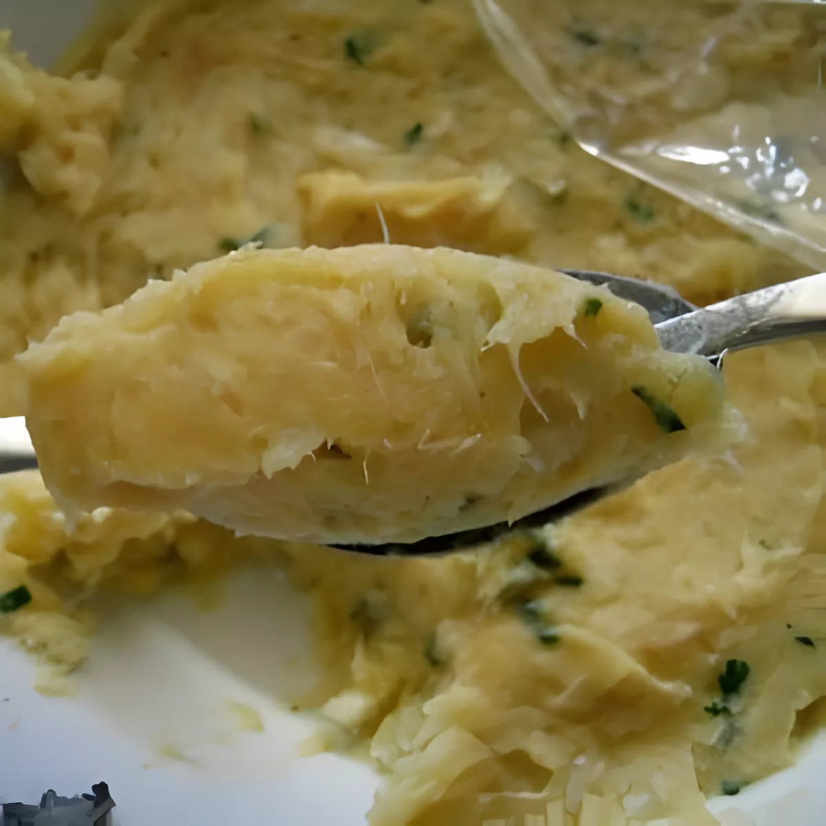 Spoonful of soft Pasteis de Bacalhau mixture showing shredded cod and parsley.