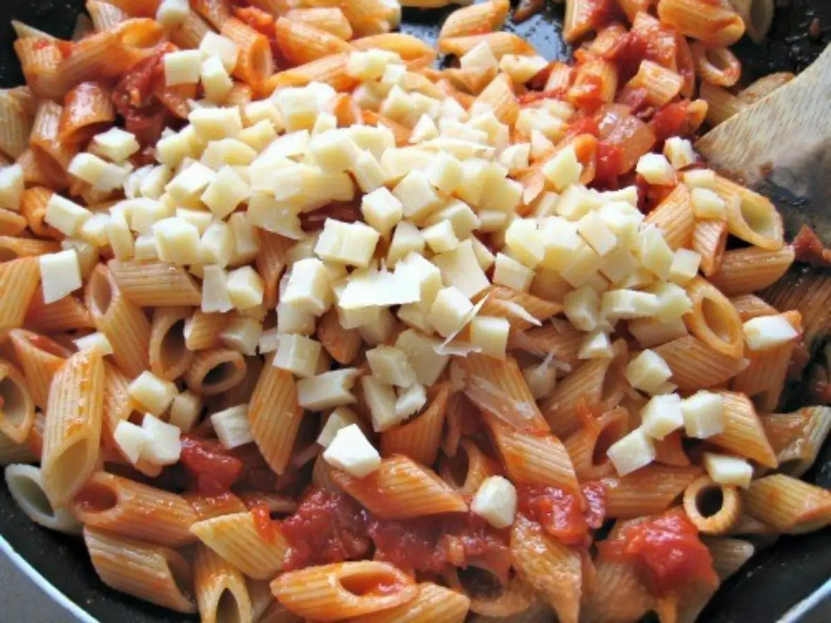 Mezze penne tossed in tomato sauce with cubes of provolone melting over the top in a wide pan.