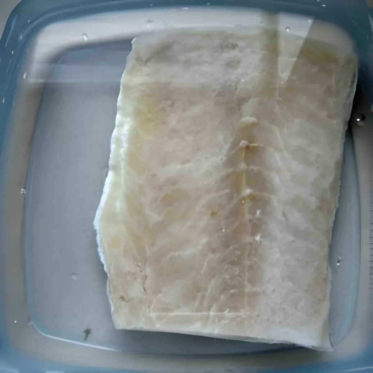 Salted cod fillet soaking in water to remove excess salt before cooking.