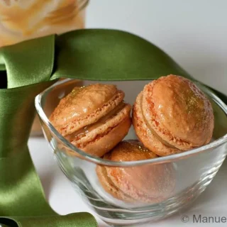 Close-up of Dulce de Leche macarons with gold dust in a glass bowl tied with a green ribbon.