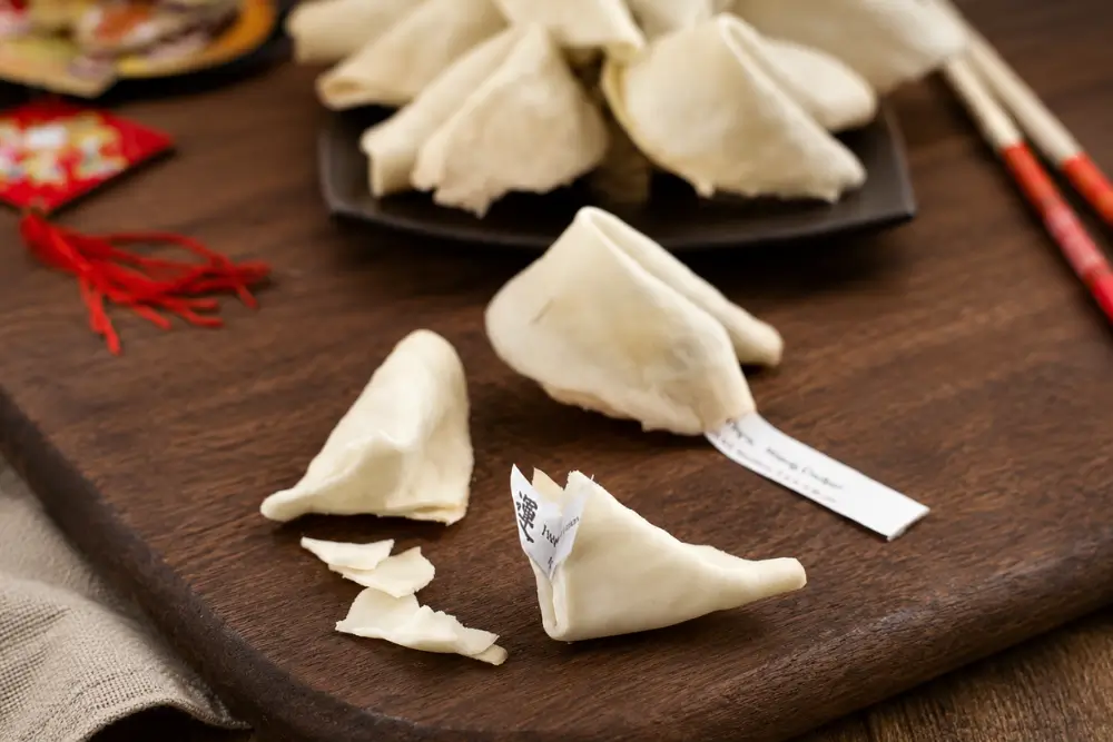 Homemade Fortune Cookies with paper fortunes peeking out on a wooden serving board.
