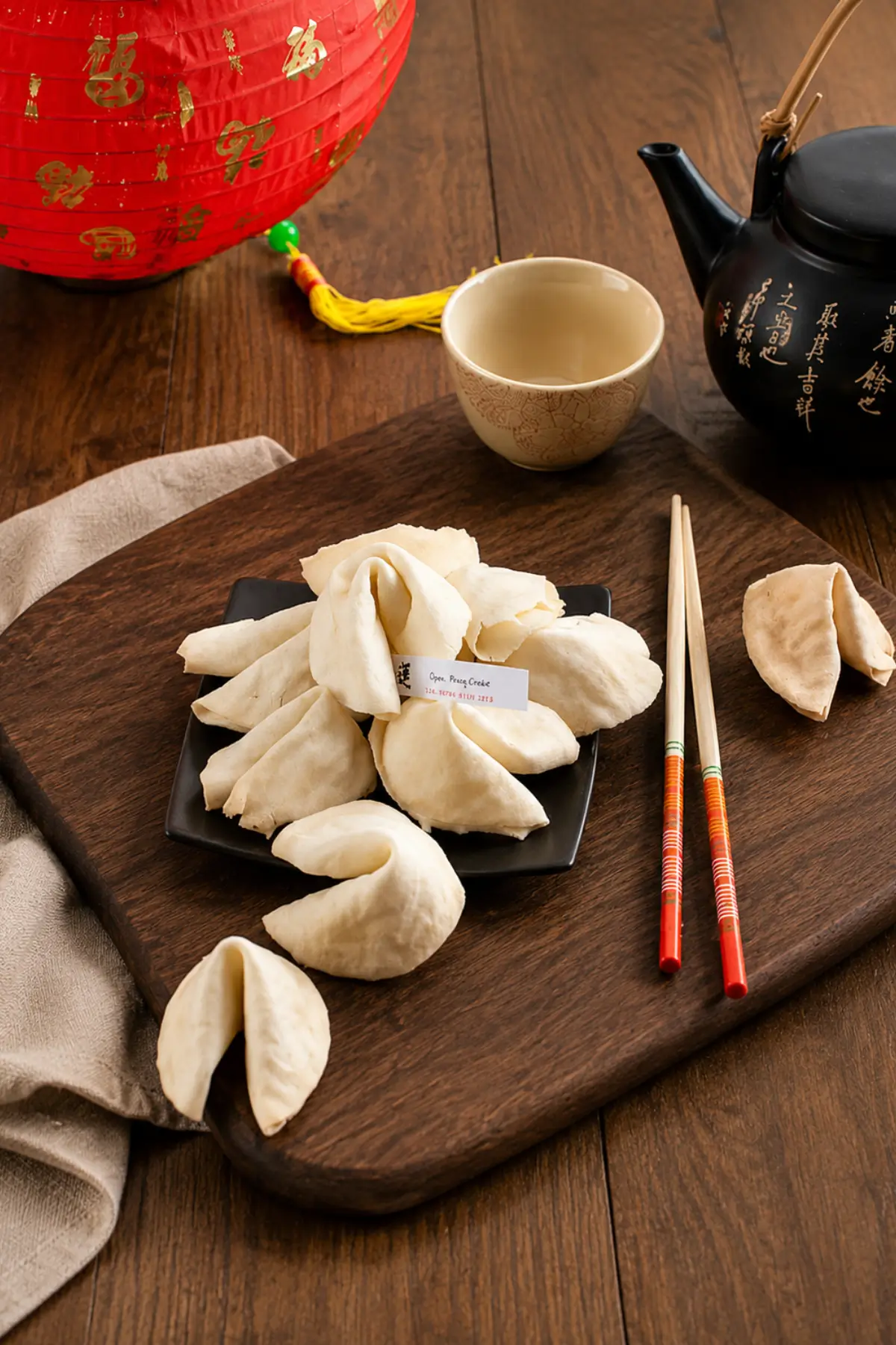 A plate of homemade fortune cookies served with chopsticks, a teapot and festive decorations.