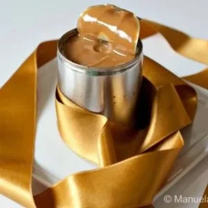 Homemade Dulce de Leche in an open tin, wrapped with a gold satin ribbon.