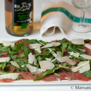 Thin slices of raw beef topped with baby rocket and Parmesan shavings on a serving plate.