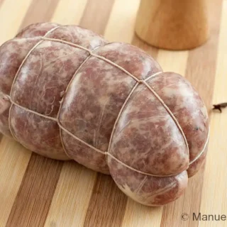 Raw Salame Cotto tied with butcher’s twine on a wooden board.