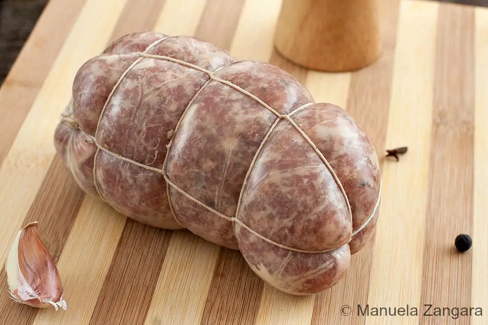 Raw Salame Cotto tied with butcher’s twine on a wooden board.