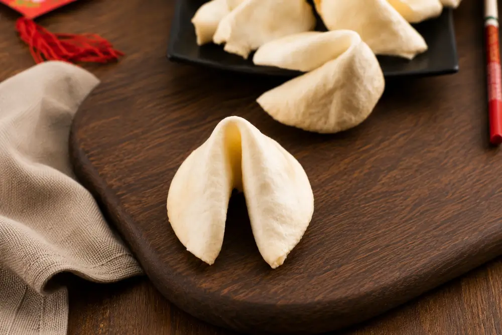 A single Fortune Cookie on a wooden serving board with more cookies blurred in the background.