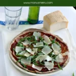 Top-down view of pizza with prosciutto, fresh rocket, and Grana slivers.