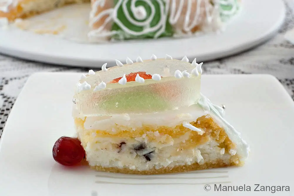 Slice of Cassata Siciliana showing layers of sponge cake, ricotta, and chocolate chips with a cherry on the side.