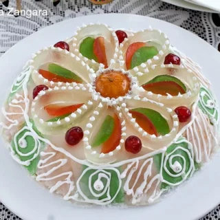 Whole Cassata Siciliana decorated with colorful candied fruits and white icing, placed on a lace tablecloth.