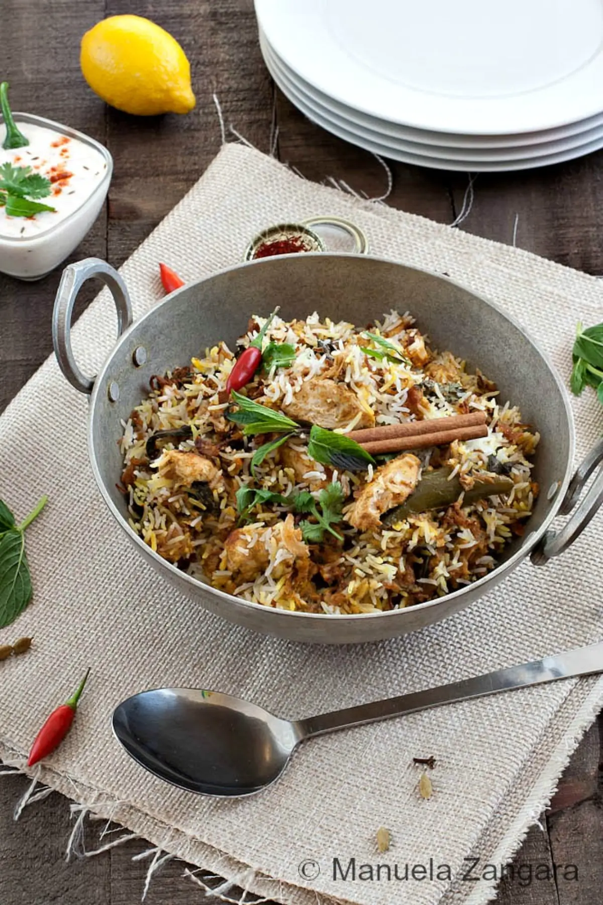 Close view of layered rice and chicken served with raita and lemon on the side.