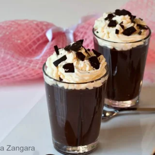 Two glasses of Chocolate Viennois with Chantilly and chocolate shards on top, set on a white plate.