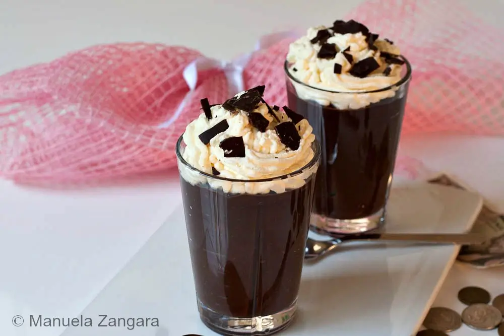 Two glasses of Chocolate Viennois with Chantilly and chocolate shards on top, set on a white plate.