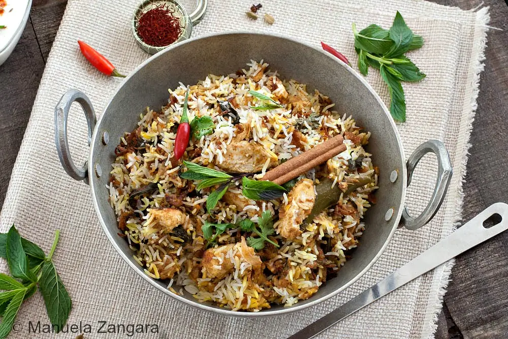 Hyderabadi Chicken Biryani served in a metal pan with fluffy basmati rice, chicken pieces, mint, and whole spices.