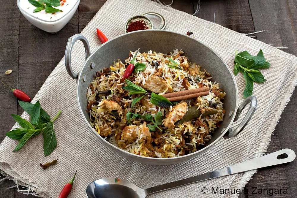 Hyderabadi Chicken Biryani served in a metal pan with fresh herbs and whole spices.