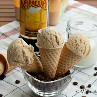 Kahlúa coffee ice cream scoops in cones with a bottle of liqueur in the background.