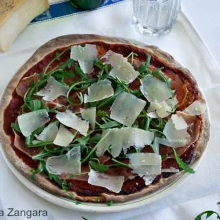 Top-down view of pizza with prosciutto, fresh rocket, and Grana slivers.