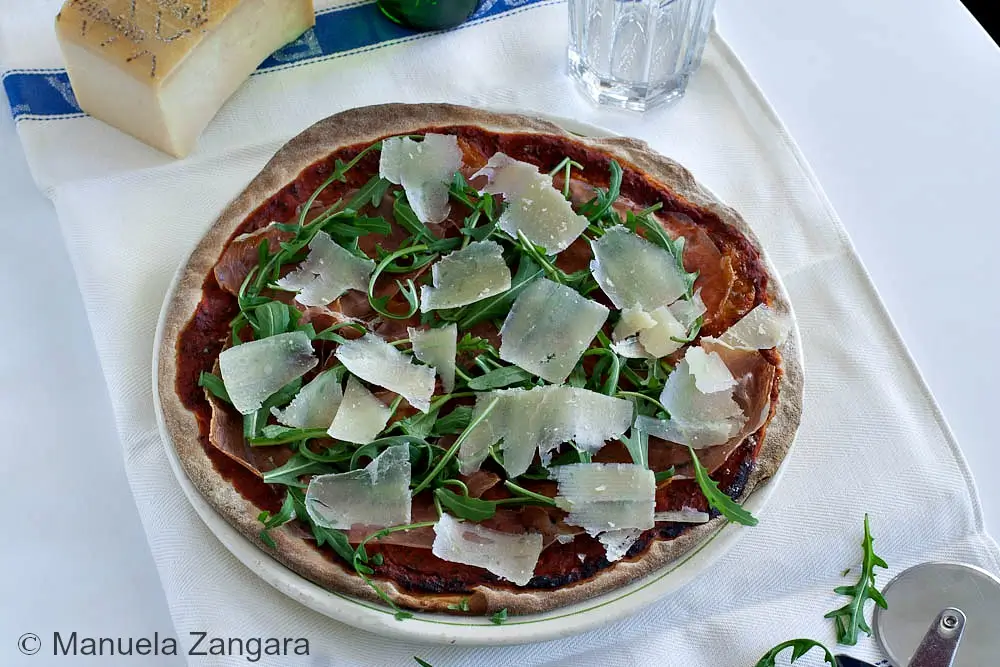 Top-down view of pizza with prosciutto, fresh rocket, and Grana slivers.