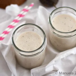 Smooth banana and coconut smoothie in glass jars with paper straws.