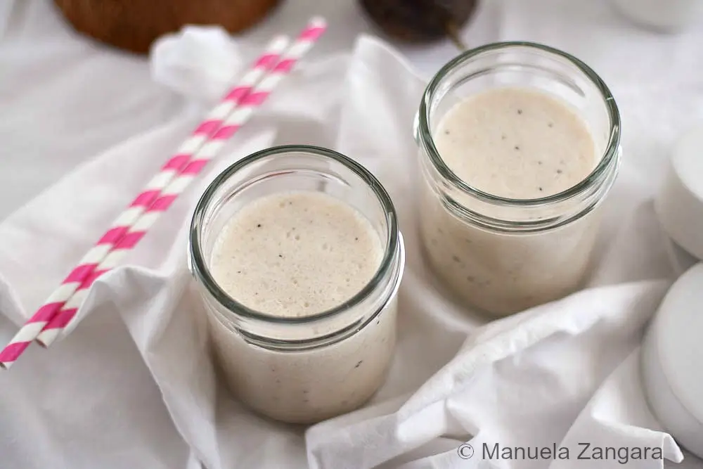Smooth banana and coconut smoothie in glass jars with paper straws.