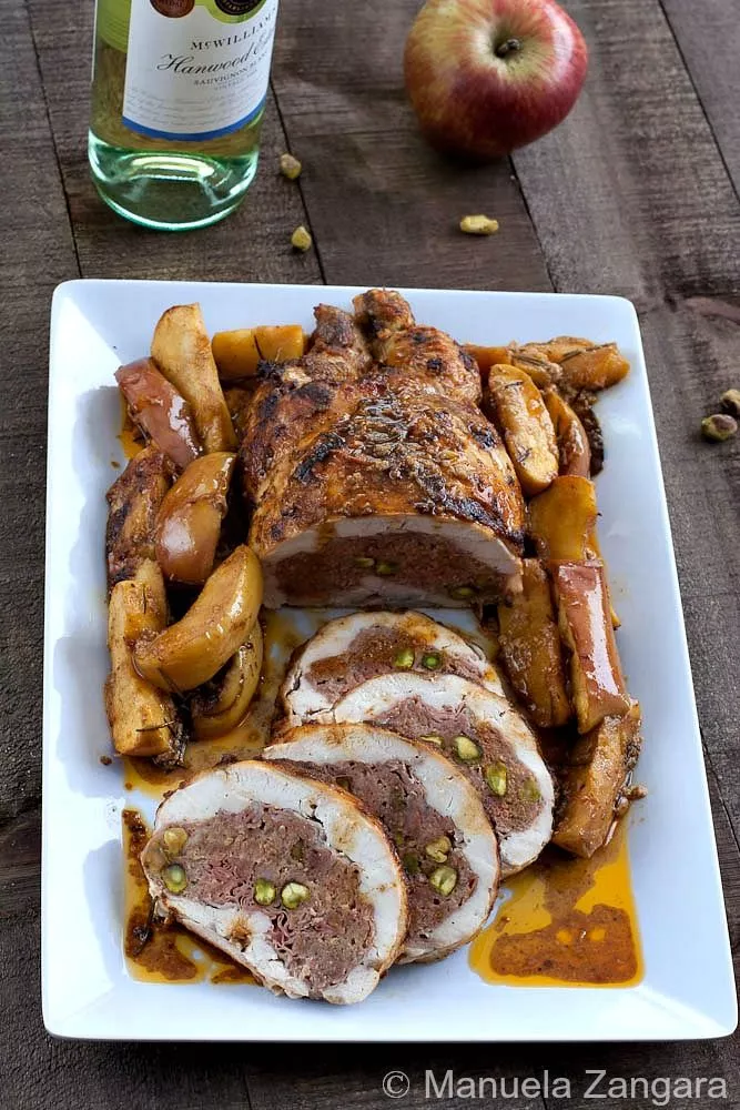 Chicken ballotine sliced and served with roasted apples and sauce on a square platter.