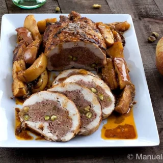 Sliced chicken ballotine filled with minced meat and pistachios served with roasted apples on a white plate.