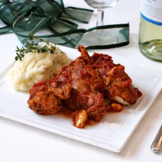 Italian rabbit stew served with mashed potatoes on a white plate with a rich tomato sauce.