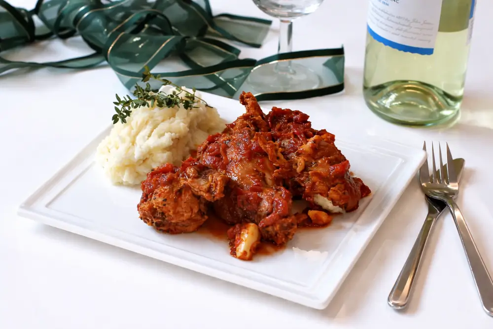 Italian rabbit stew served with mashed potatoes on a white plate with a rich tomato sauce.