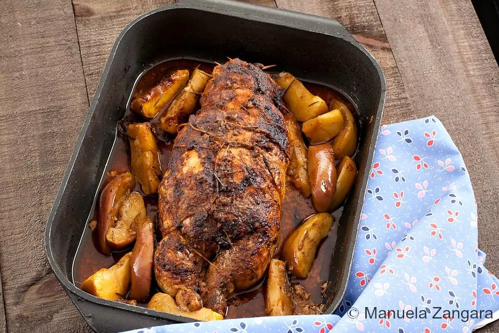 Roasted chicken ballotine with golden skin and apple wedges in a baking pan after cooking.